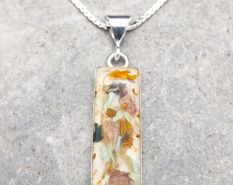 Op de afbeelding: Een zilveren ketting met een rechthoekige hanger met geperste bloemen en bladeren ingekapseld in helder hars.