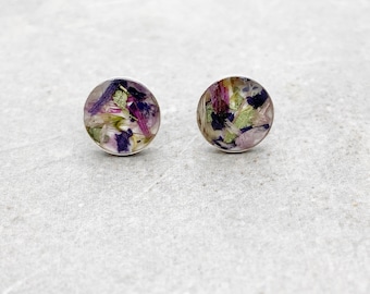 May include: A pair of silver stud earrings with a round, clear resin design featuring pressed purple, pink, and green flowers.