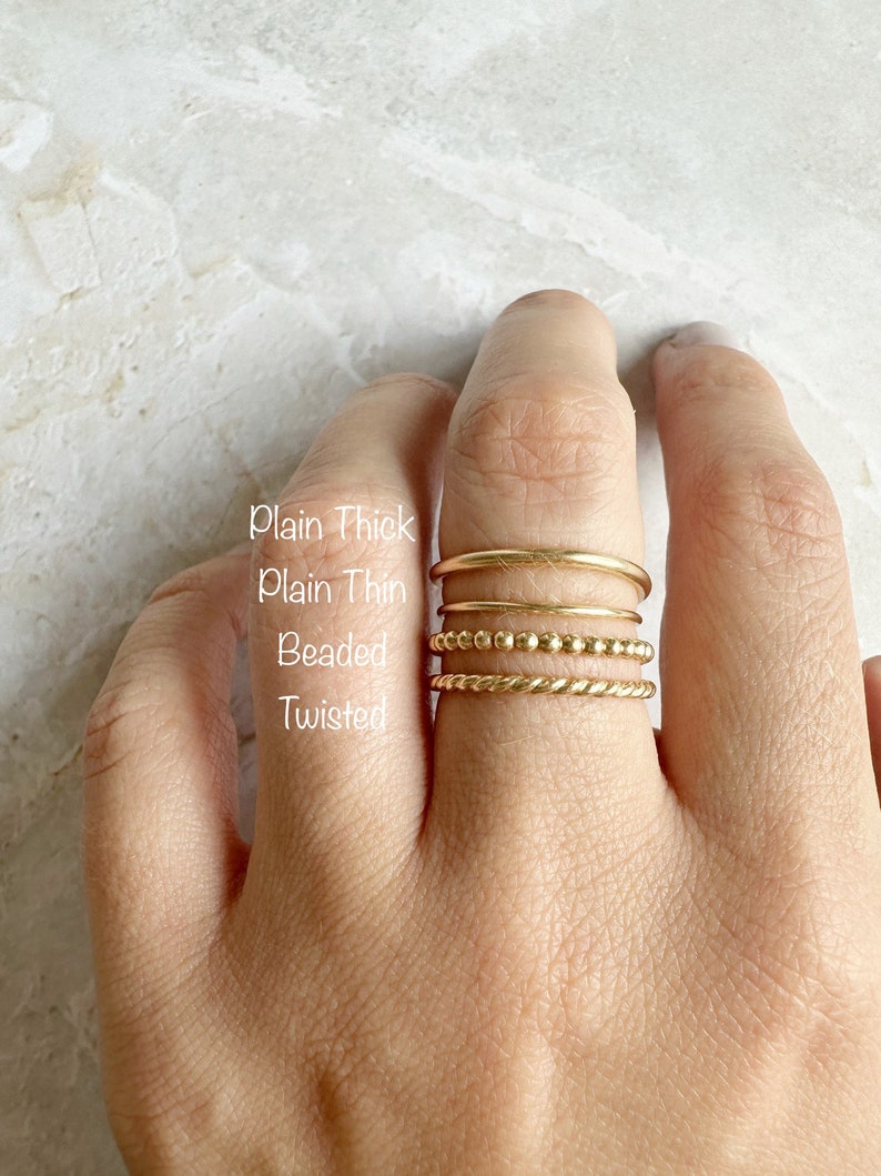 以下が含まれることがあります： 指に重ねられた4つの金のリング。リングには「Plain Thick」、「Plain Thin」、「Beaded」、「Twisted」とラベルが付けられています。