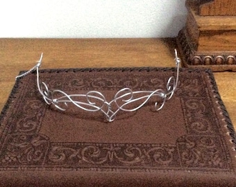 May include: A silver wire headband with a delicate, intricate design. The headband is shaped like a crown with a heart-shaped center.