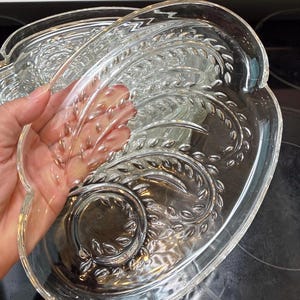 Peut inclure: Un plat de service en verre transparent présentant un motif en relief de tiges de blé texturées sur la surface. L'objet possède une forme organique incurvée avec un bord lisse et une section centrale circulaire, offrant une finition transparente.