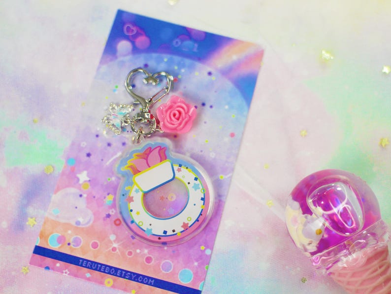 May include: A pink and white keychain charm with a flower and a life preserver design. The charm is attached to a silver key ring with a heart-shaped charm. The background is a rainbow gradient with glitter.