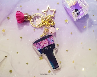 May include: A black and purple light stick keychain with a pink heart and a pink tassel charm. The keychain also features a gold star charm, a pearl and gold chain, and a pink bead.