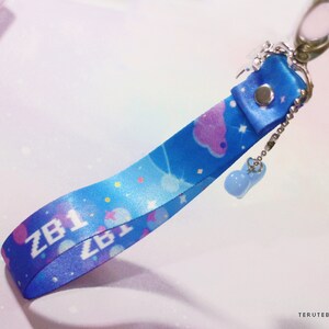 May include: A blue and white lanyard with a star and cloud pattern. The lanyard has the text "ZB1" printed on it and a small blue charm attached to it.