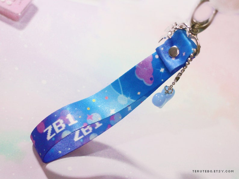 May include: A blue and white lanyard with a star and cloud pattern. The lanyard has the text "ZB1" printed on it and a small blue charm attached to it.