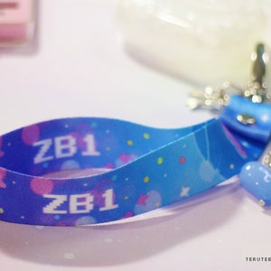 May include: A blue and pink patterned lanyard with the text "ZB1" printed on it. The lanyard has a blue heart charm attached to it.