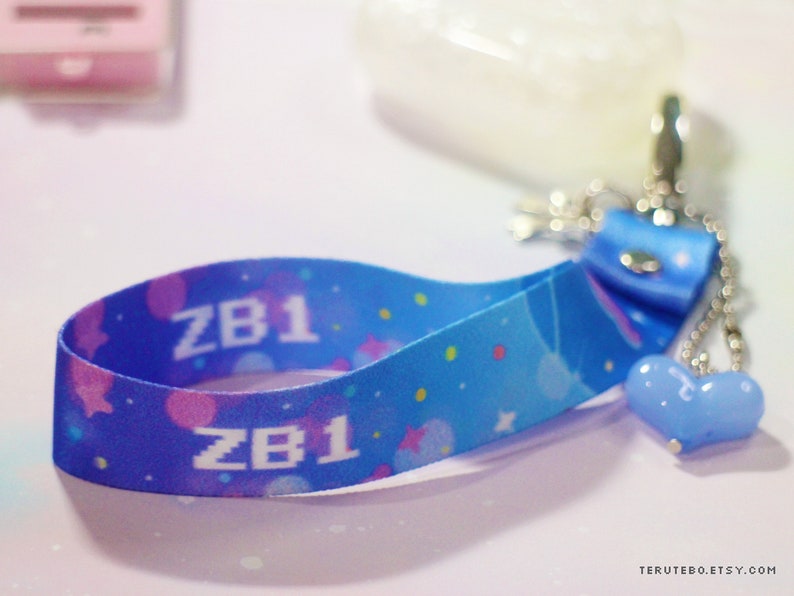 May include: A blue and pink patterned lanyard with the text "ZB1" printed on it. The lanyard has a blue heart charm attached to it.