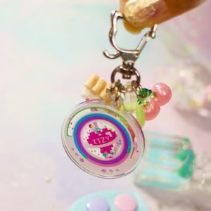 May include: A handmade wooden sign with the text "Welcome" in a playful font. The sign is painted white with a distressed finish, and features a decorative floral design in shades of pink and green. It measures approximately 12 inches wide.