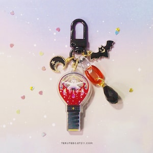 May include: A red and white light-up keychain with a black handle, a crescent moon charm, a black bat charm, and a red and black bead charm. The keychain is attached to a black metal clip.