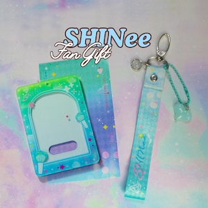 Puede incluir: Un tarjetero rectangular de color turquesa y azul con una ventana central clara y una correa de muñeca a juego. El conjunto presenta pequeños gráficos de estrellas y diamantes, el texto SHINee Fan Gift y un pequeño dije de corazón azul.