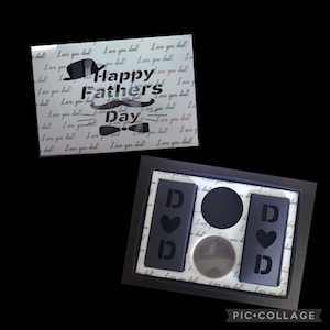 May include: A black gift box with a white background and the text "Happy Father's Day" in a decorative font. The box contains three black gift boxes with the letter "D" and a heart on each.