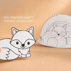 Può includere: Carta artigianale fai-da-te con un'illustrazione di una volpe bianca. La volpe è mostrata in due pose: una seduta e una che dorme in una tana. Il testo "DIY Papercraft Instant Download" è in alto.
