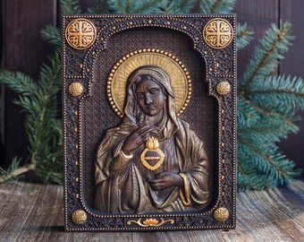Puede incluir: Un icono de madera que representa a la Virgen María con un corazón de oro en sus manos. El icono está enmarcado en madera oscura con detalles dorados y tallas intrincadas.