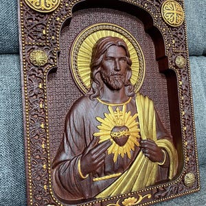 K&ouml;nnte beinhalten: Eine rechteckige Wandplatte aus Holz mit einem geschnitzten Relief des Heiligsten Herzens Jesu. Die Figur ist mit einem goldenen Heiligenschein und einem strahlenden Herzen dargestellt, vor einem dunkelbraunen Hintergrund mit floralen Details.