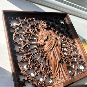 Puede incluir: Una escultura de pared de madera de una figura religiosa con un coraz&oacute;n en la mano, tallada en un estilo g&oacute;tico detallado.