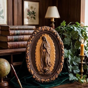May include: An oval, wooden religious plaque featuring a carved image of the Virgin Mary. The plaque is framed with a floral border and rests on a dark green cloth. The background includes books, a globe, and a lit candle.