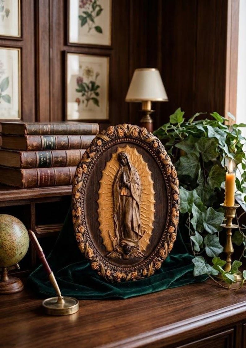 May include: An oval, wooden religious plaque featuring a carved image of the Virgin Mary. The plaque is framed with a floral border and rests on a dark green cloth. The background includes books, a globe, and a lit candle.