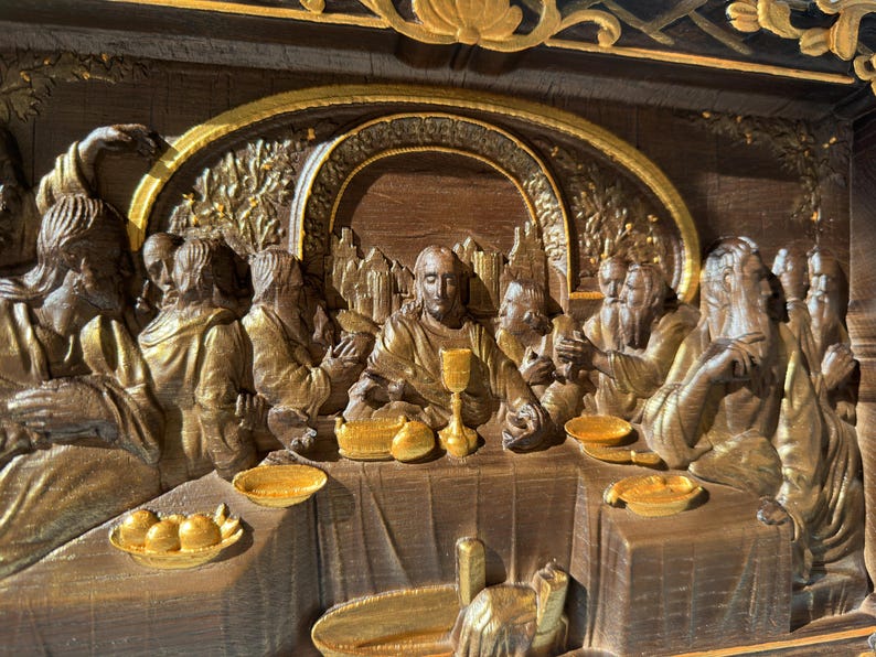 May include: A wooden relief sculpture depicting the Last Supper. The figures are carved in a realistic style and are painted in shades of brown and gold. The scene is set in a room with a table and chairs. The figures are seated around the table, and Jesus is in the center.