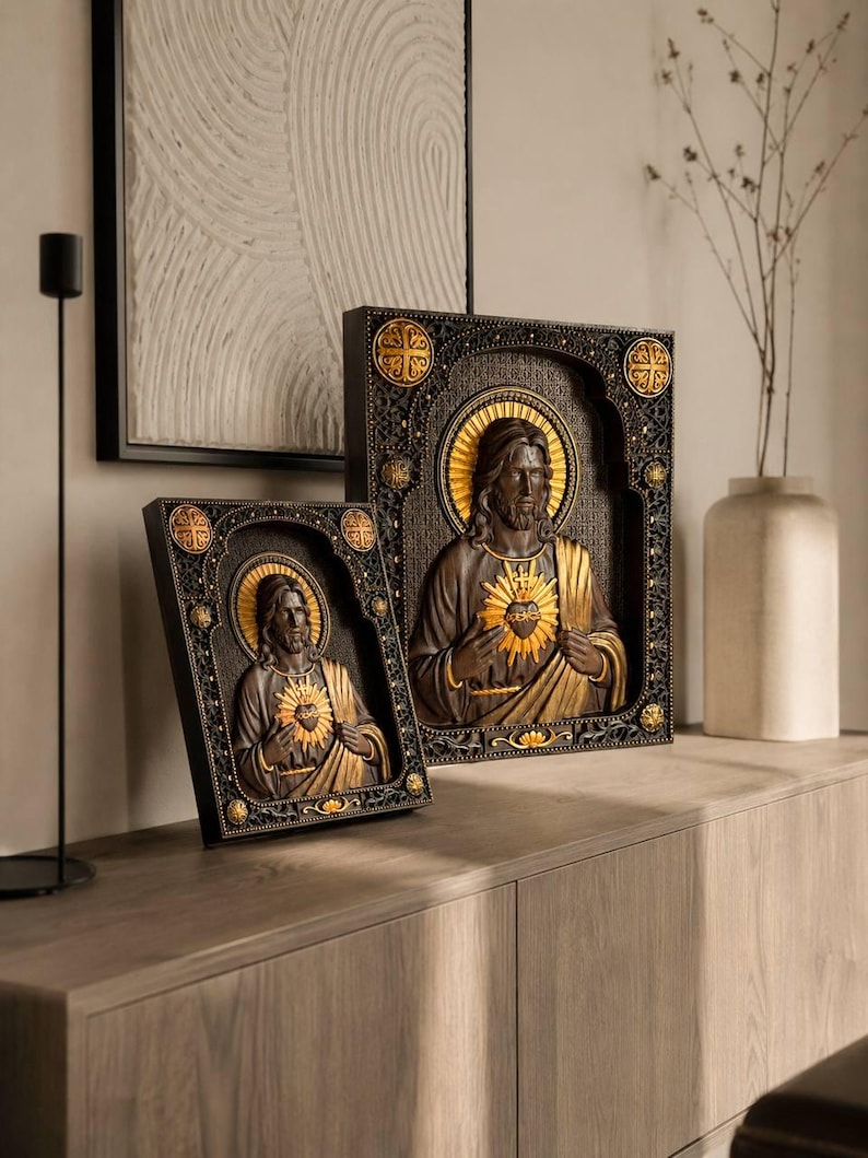 K&ouml;nnte beinhalten: Zwei rechteckige Wandtafeln mit einem Relief des Heiligsten Herzens Jesu. Die Figuren sind in Dunkelbraun und Gold gehalten und in aufwendige schwarze Rahmen mit goldenen kreisf&ouml;rmigen Akzenten an den Ecken und Seiten eingefasst.