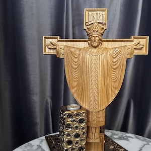 Może przedstawiać: Drewniany krucyfiks z szczeg&oacute;łową rzeźbą postaci z wyciągniętymi ramionami, w koronie i szatach. Krzyż ma napis "INRI" u g&oacute;ry. Złoty świecznik znajduje się poniżej.