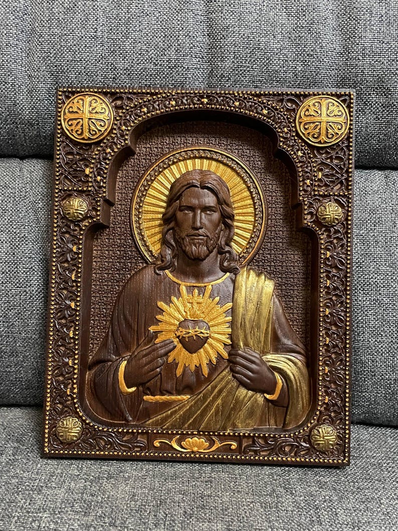 K&ouml;nnte beinhalten: Eine rechteckige Wandtafel aus Holz mit einem geschnitzten Relief des Heiligsten Herzens Jesu. Die Figur ist mit langem Haar, Bart und einem goldenen Heiligenschein dargestellt. Der Rahmen ist dunkelbraun mit floralen Schnitzereien.