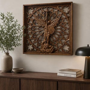 May include: A square wooden wall art piece featuring a detailed relief carving of an angel holding a cross and shield, set against an intricate gothic-style circular lattice pattern with open cutouts, framed in a dark brown wood border.