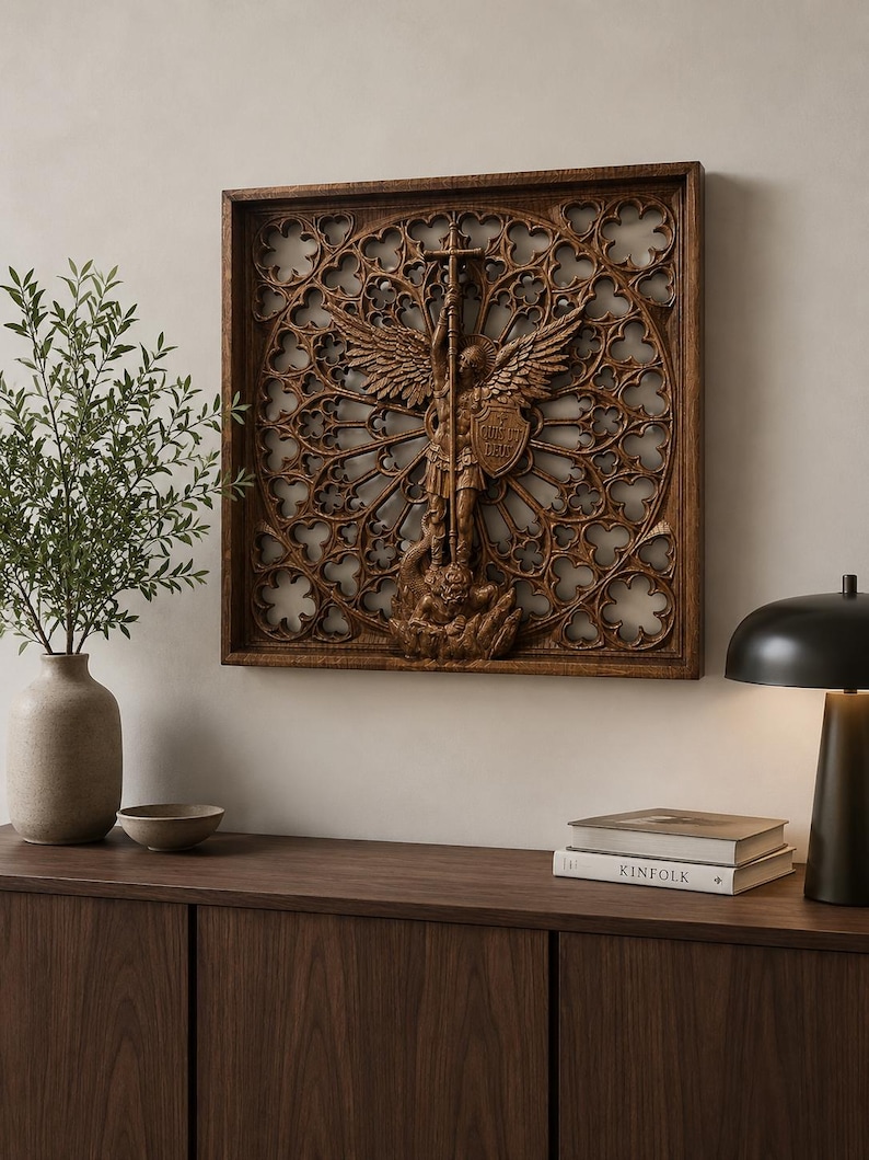May include: A square wooden wall art piece featuring a detailed relief carving of an angel holding a cross and shield, set against an intricate gothic-style circular lattice pattern with open cutouts, framed in a dark brown wood border.