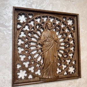 Puede incluir: Una pieza de arte de pared de madera con una imagen tallada de Jes&uacute;s con un coraz&oacute;n en la mano. La talla est&aacute; sobre un fondo de un dise&ntilde;o de ventana de vitral circular detallado e intrincado.