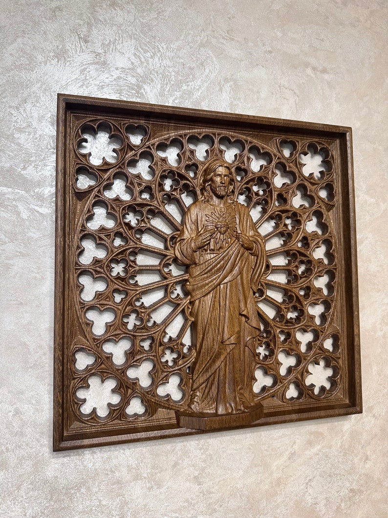Puede incluir: Una pieza de arte de pared de madera con una imagen tallada de Jes&uacute;s con un coraz&oacute;n en la mano. La talla est&aacute; sobre un fondo de un dise&ntilde;o de ventana de vitral circular detallado e intrincado.