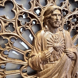 Puede incluir: Una talla de madera de Jesucristo con un coraz&oacute;n en el pecho, rodeada de un marco de madera tallado decorativo e intrincado.