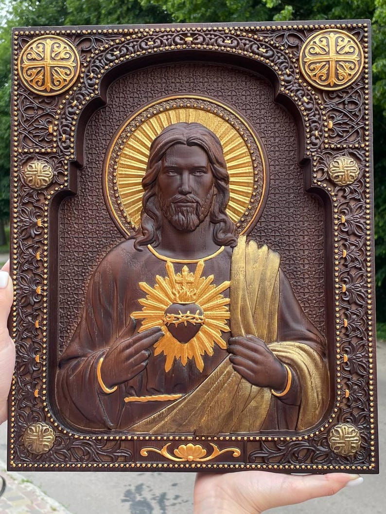 K&ouml;nnte beinhalten: Eine rechteckige Wandtafel aus dunkelbraunem Holz mit einem geschnitzten Relief des Heiligsten Herzens Jesu. Die Figur hat einen goldenen Heiligenschein und ein goldenes Herz mit Dornenkrone. Der Rahmen ist mit komplexen Mustern und Gold verziert.