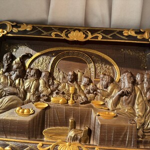 May include: A framed, 3D relief sculpture depicting the Last Supper. The scene is set in a dark wood frame with gold accents. The figures are sculpted in a realistic style and are painted in shades of brown and gold.