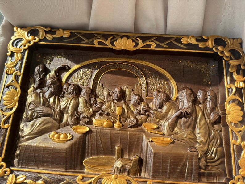 May include: A framed, 3D relief sculpture depicting the Last Supper. The scene is set in a dark wood frame with gold accents. The figures are sculpted in a realistic style and are painted in shades of brown and gold.