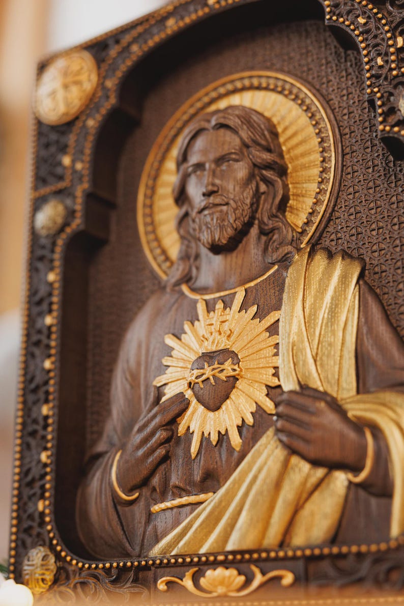 K&ouml;nnte beinhalten: Eine Wandtafel aus dunklem Holz mit einem geschnitzten Relief von Jesus Christus, einem goldenen Heiligenschein und einem goldenen Herz-Jesu-Emblem. Die Figur hat langes Haar und einen Bart und tr&auml;gt ein drapiertes Gewand mit Goldakzenten.
