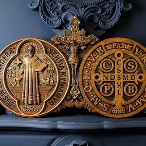 May include: Two wooden plaques with religious imagery. The left plaque features a depiction of Saint Benedict with the words "EIVS IN OBITVNRO PR&AElig;" and "EX SM CASINO MDCCCLXXX". The right plaque features a depiction of the Saint Benedict Medal with the words "PAX" and "V.R.S.N.S.V.B.B.V.I.T.O.M.N.S.S.M.W."