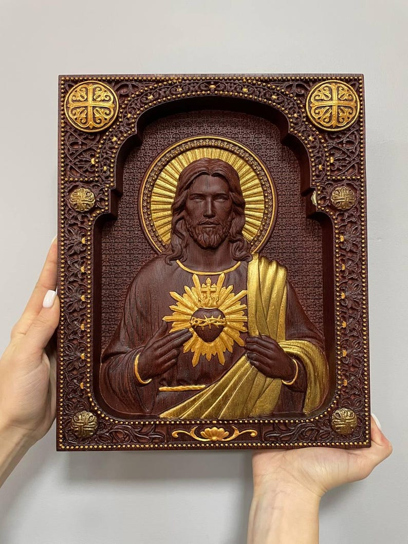 K&ouml;nnte beinhalten: Eine rechteckige Wandtafel aus Holz mit einem geschnitzten Relief des Heiligsten Herzens Jesu. Die Figur ist mit einem goldenen Heiligenschein und einem goldenen Herzsymbol dargestellt. Der Rahmen ist detailliert mit dunklem Holz und Gold.