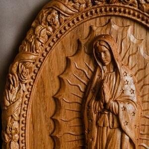 May include: A detailed wooden carving of a religious figure, featuring an oval frame with floral and beaded accents. The central figure is depicted with hands clasped in prayer, wearing a draped garment adorned with stars. The carving is in shades of brown.