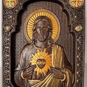 K&ouml;nnte beinhalten: Eine rechteckige Wandtafel aus dunklem Holz mit einem geschnitzten Relief von Jesus Christus, einem goldenen Heiligenschein und dem Heiligsten Herzen. Der Rahmen ist detailliert mit dunklen Holzschnitzereien und goldenen Akzenten verziert.