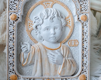 May include: White wooden icon with a gold-painted frame and details. The icon depicts a young boy with a halo, wearing a white robe with gold accents. The text "IC XC" is visible on the icon.