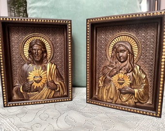 Puede incluir: Dos iconos religiosos enmarcados en madera con detalles dorados. El icono de la izquierda representa a Jesús con un corazón dorado y el icono de la derecha representa a María con un corazón dorado.