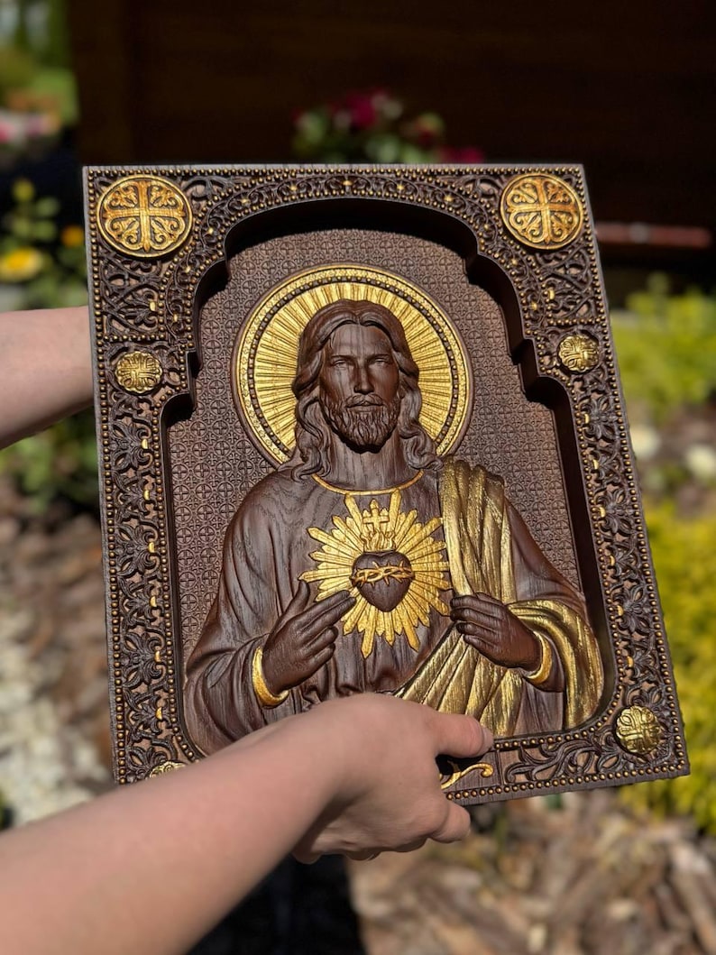 K&ouml;nnte beinhalten: Eine rechteckige Wandtafel aus Holz mit einem geschnitzten Relief des Heiligsten Herzens Jesu. Die Figur hat einen goldenen Heiligenschein und ein goldenes Herz, mit dunklen Holzt&ouml;nen und kunstvollen floralen Randverzierungen.