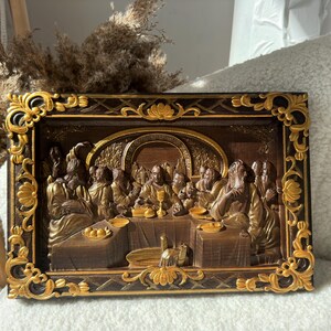 May include: A framed wood carving depicting the Last Supper. The carving is painted in gold and brown tones and features a detailed depiction of Jesus and his disciples.