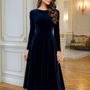 May include: A navy blue velvet dress with long sleeves and a flared skirt. The dress features a round neckline and reaches the mid-calf. The woman is wearing gold heels. The background is a room with decorative architectural features.