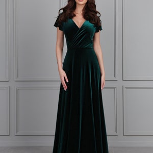 Peut inclure: Une longue robe en velours vert foncé avec un décolleté en V et des manches courtes. La robe a un corsage style cache-cœur et une jupe fluide.