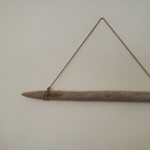May include: A piece of driftwood is hanging from a wall using a simple rope. The driftwood is light brown and has a natural, rough texture.