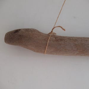 Könnte beinhalten: Ein Stück Treibholz mit einer natürlichen, rauen Textur, das mit Schnur gebunden ist. Das Holz ist hellbraun und hat eine leicht gebogene Form.