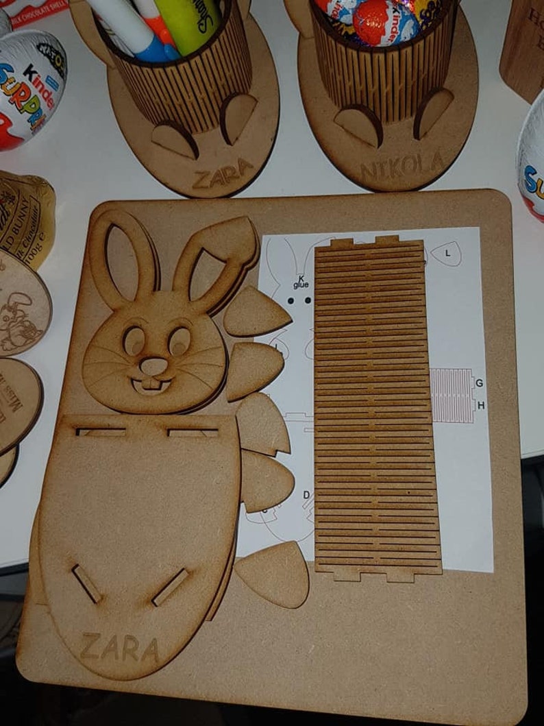 May include: A wooden Easter bunny craft kit with the name "ZARA" engraved on the front. The kit includes a bunny shaped box, a separate piece for the back of the box, and a sheet of instructions with the letters "G", "H", "L", and "K glue" printed on it.