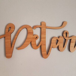 Puede incluir: Un letrero de madera con la palabra "Petar" escrita en letra cursiva.