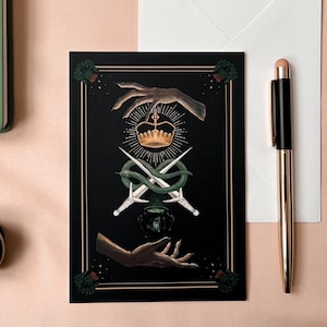 Illustrated Macbeth postcard
picturing witchy hands, golden crown, a snake wrapped around two daggers, and a couldron. There is a thistle in each corner, and two golden lines decorating all 4 sides of the card.

Comes with a white envelope.