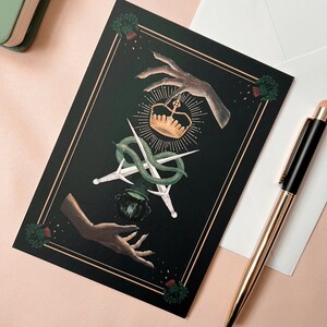 Illustrated Macbeth postcard
picturing witchy hands, golden crown, a snake wrapped around two daggers, and a couldron. There is a thistle in each corner, and two golden lines decorating all 4 sides of the card.